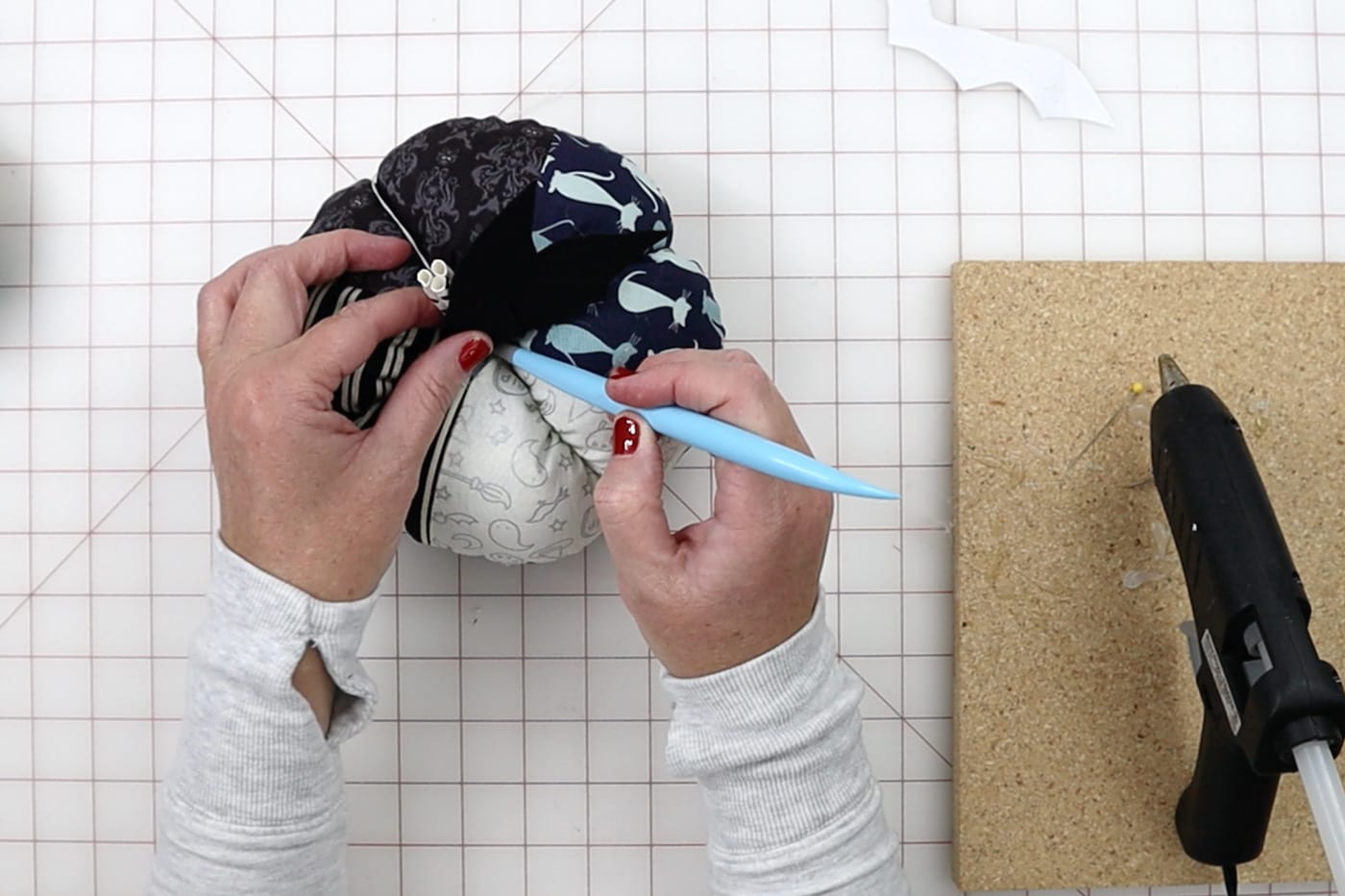 mains construisant une citrouille en tissu avec des outils sur un tapis de découpe blanc