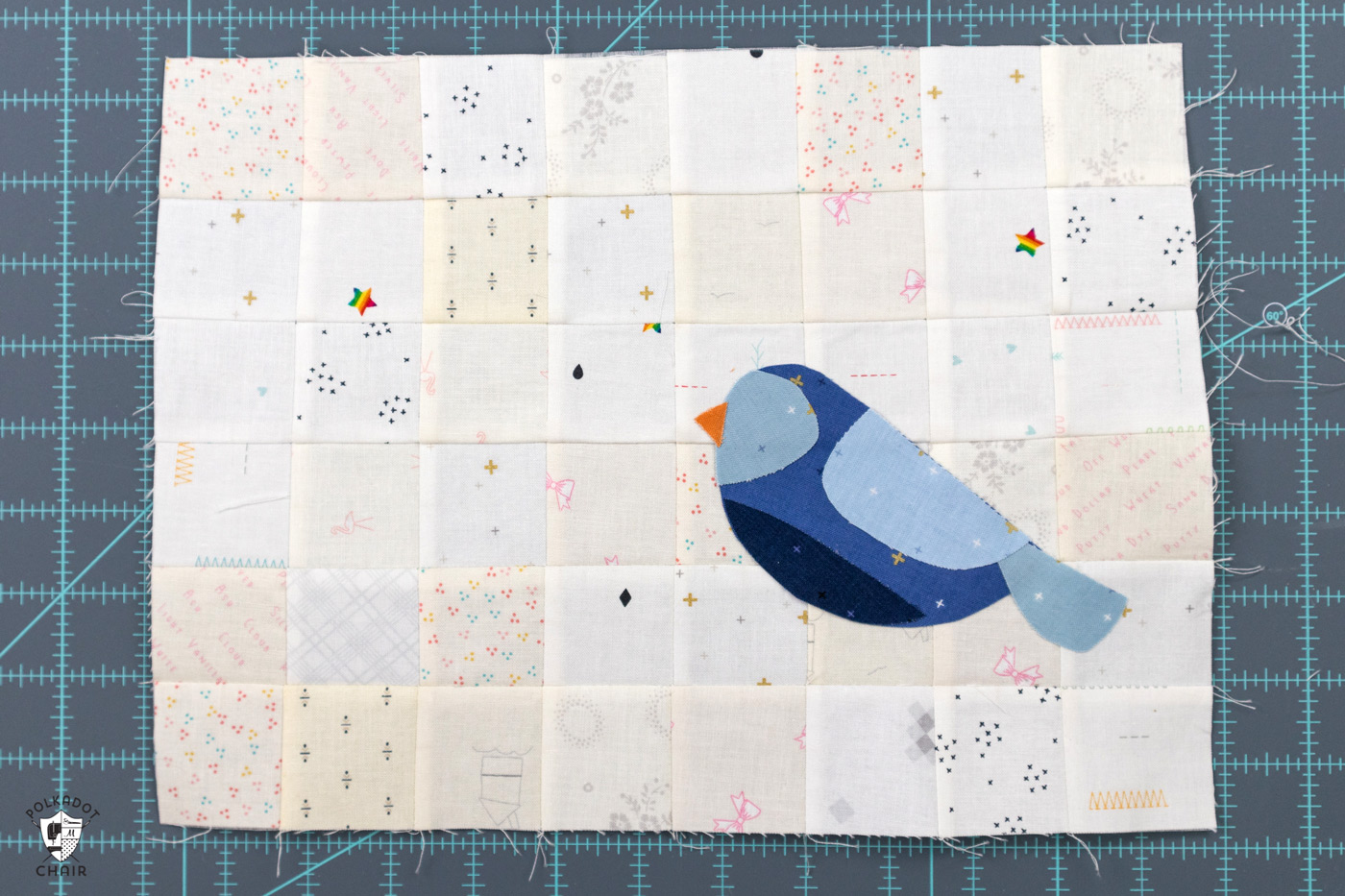 oiseau bleu cousu sur une grille patchwork de carrés blancs et crème