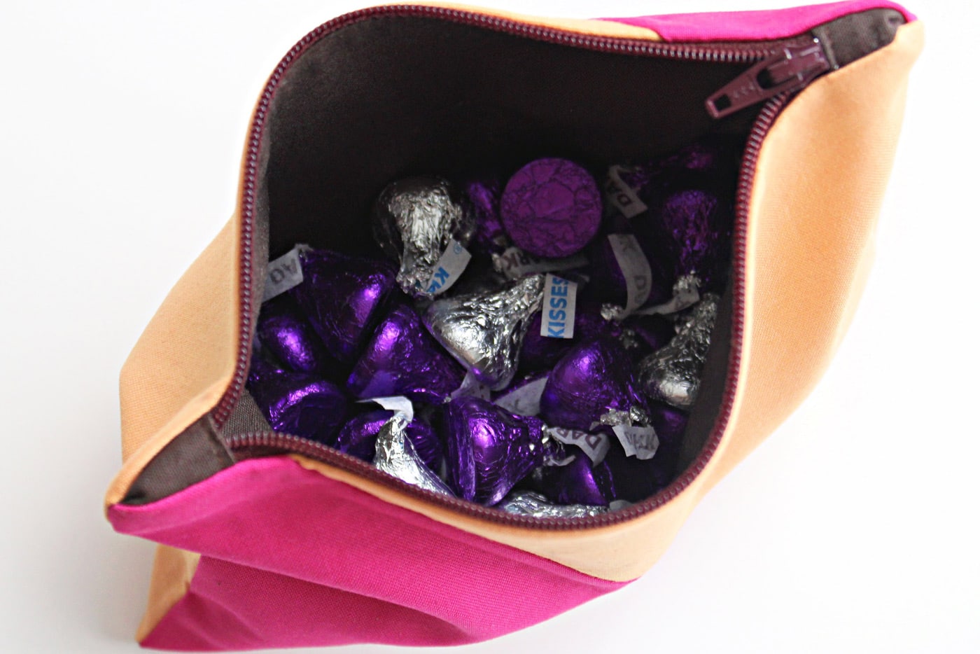 Pochette zippée rose et pêche avec applique baiser au chocolat et bonbons au chocolat sur table blanche