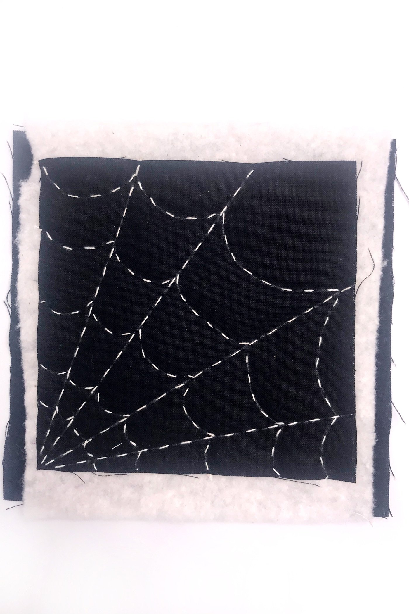 tissu noir avec une toile d'araignée blanche cousue avec du fil blanc sur une table blanche