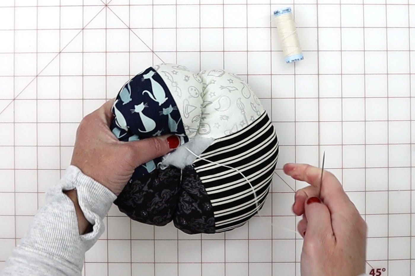 mains construisant une citrouille en tissu avec des outils sur un tapis de découpe blanc