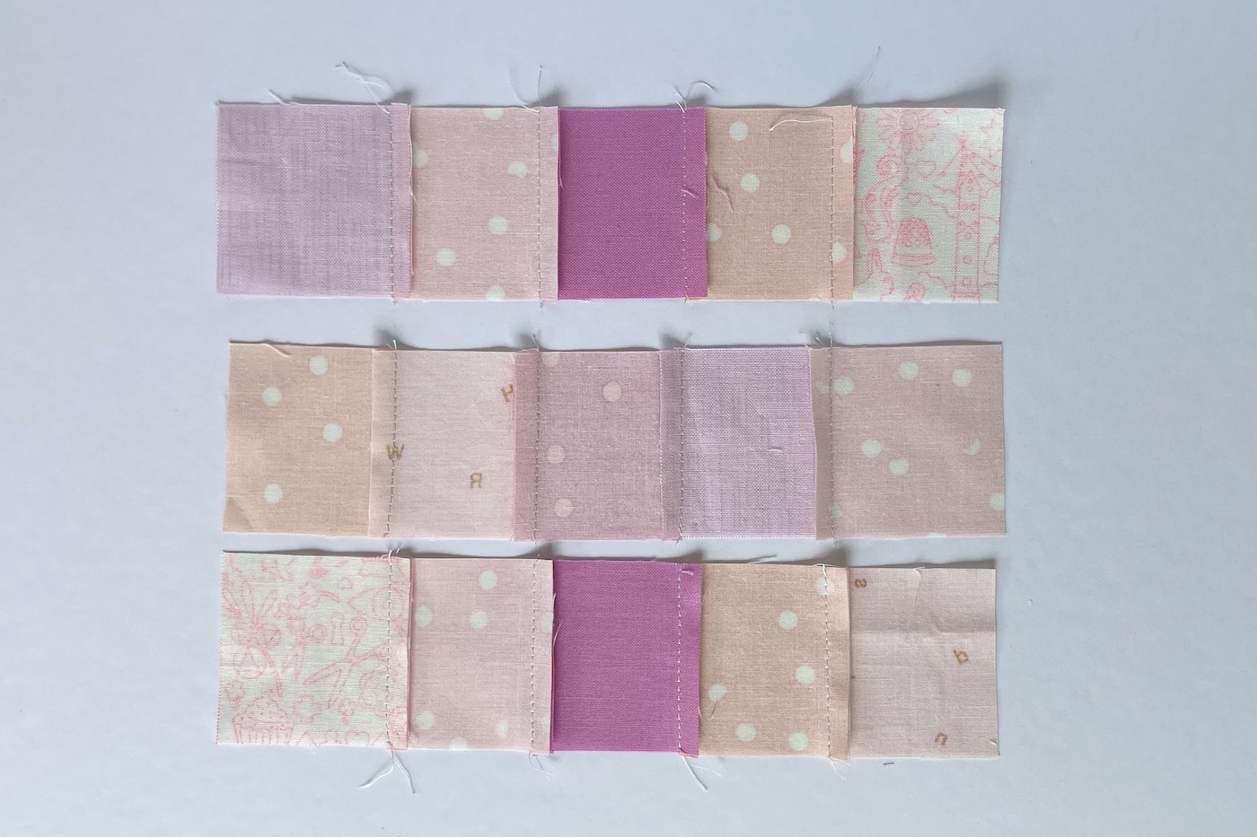 carrés de tissu rose cousus ensemble sur une table blanche
