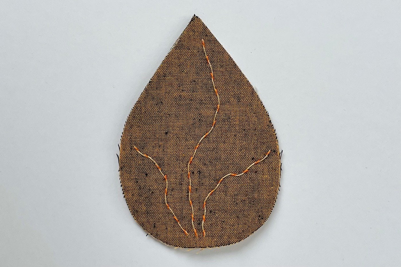 feuille de tissu marron avec aiguille et fil sur table blanche