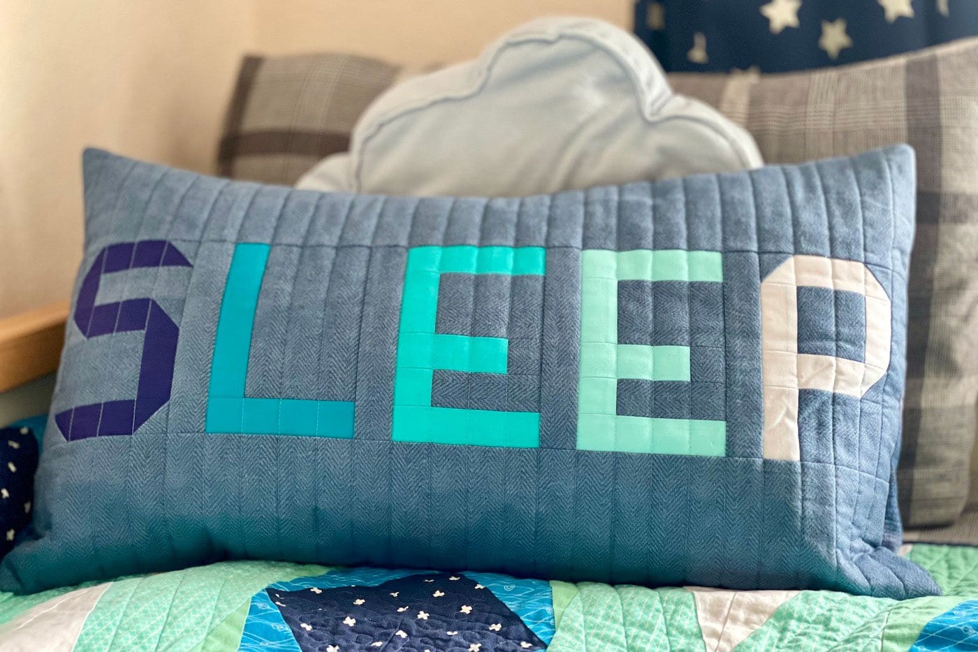 oreiller patchwork bleu et gris sur le lit avec d'autres oreillers