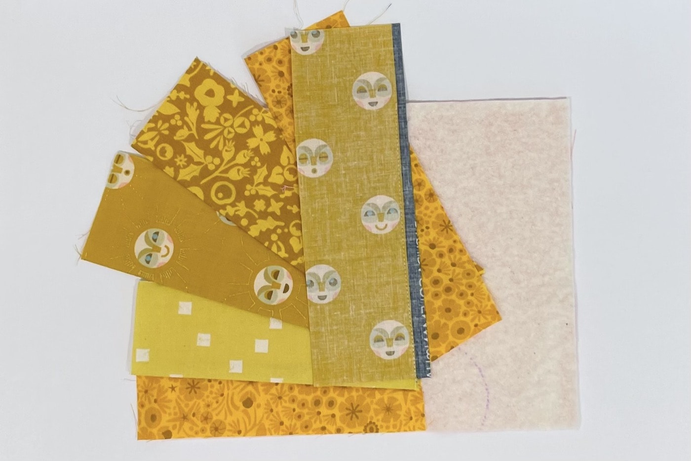 étapes de construction d'un tapis mug avec des bandes de divers imprimés de tissus jaunes sur une table blanche