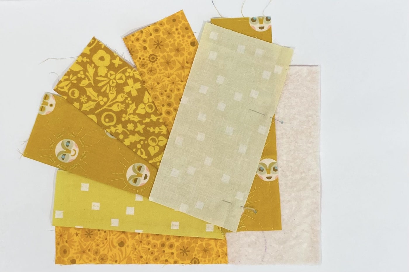 étapes de construction d'un tapis mug avec des bandes de divers imprimés de tissus jaunes sur une table blanche
