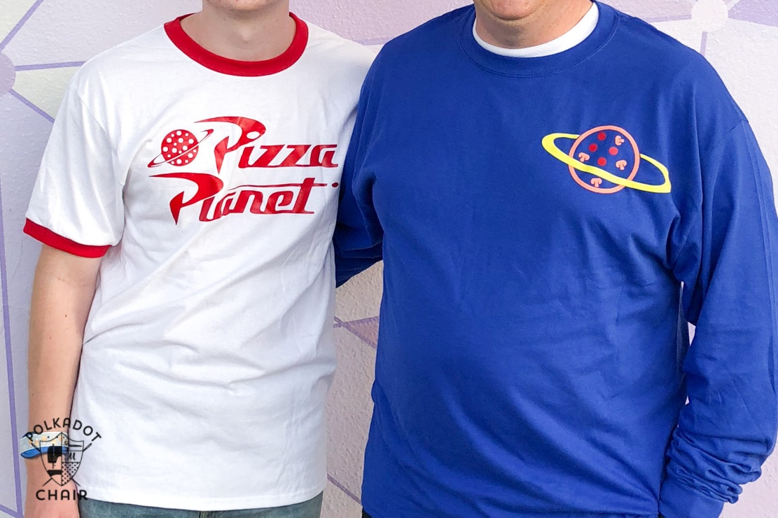 Zoom sur deux t-shirts pour hommes. L’un est blanc avec une doublure rouge sur le col et la manche avec le logo Pizza Planet. L'autre porte un t-shirt bleu foncé à manches longues avec une pizza entourée d'un anneau dans le coin supérieur.