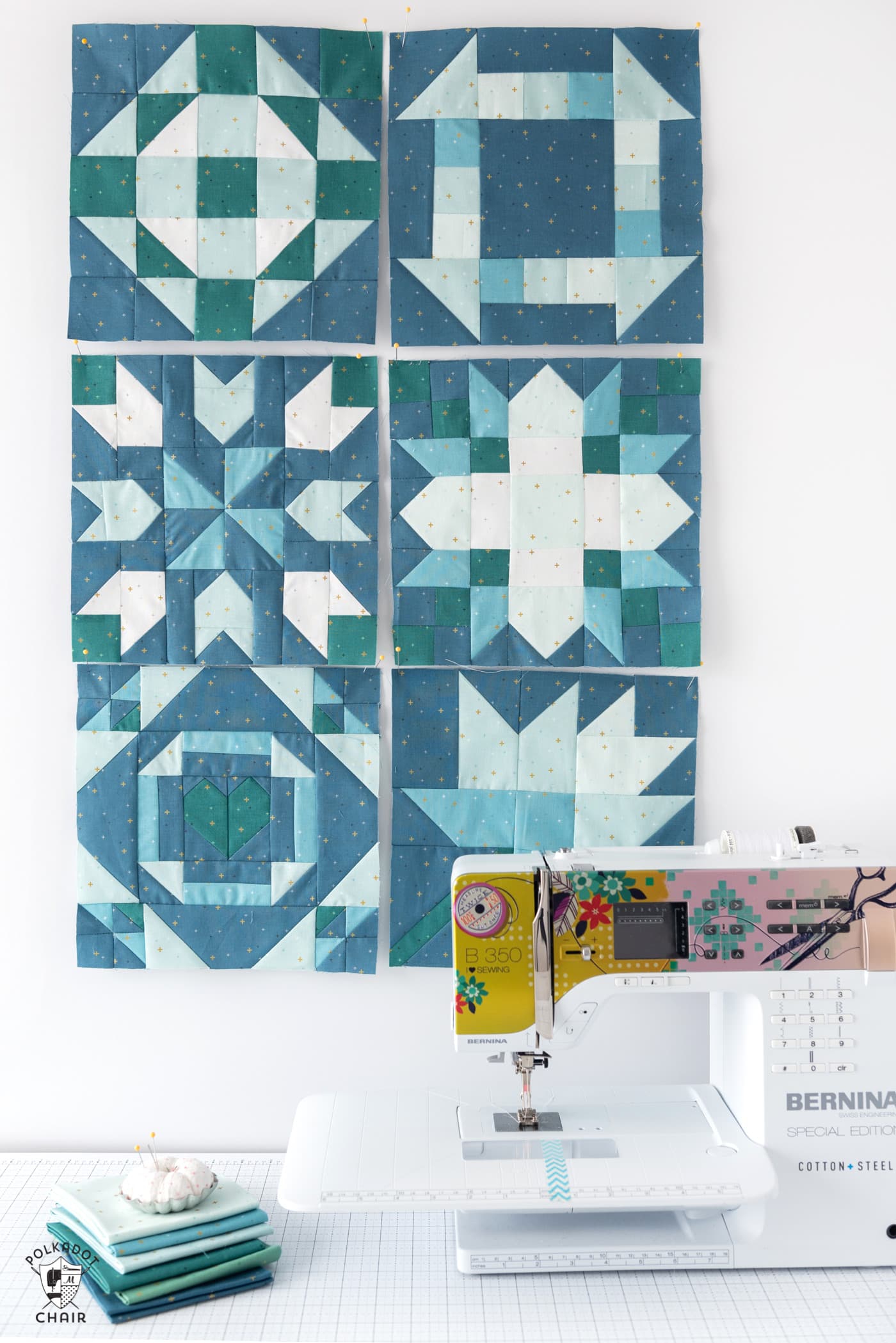 Zes blauwe en aquakleurige quiltblokken op een witte muur voor de naaimachine