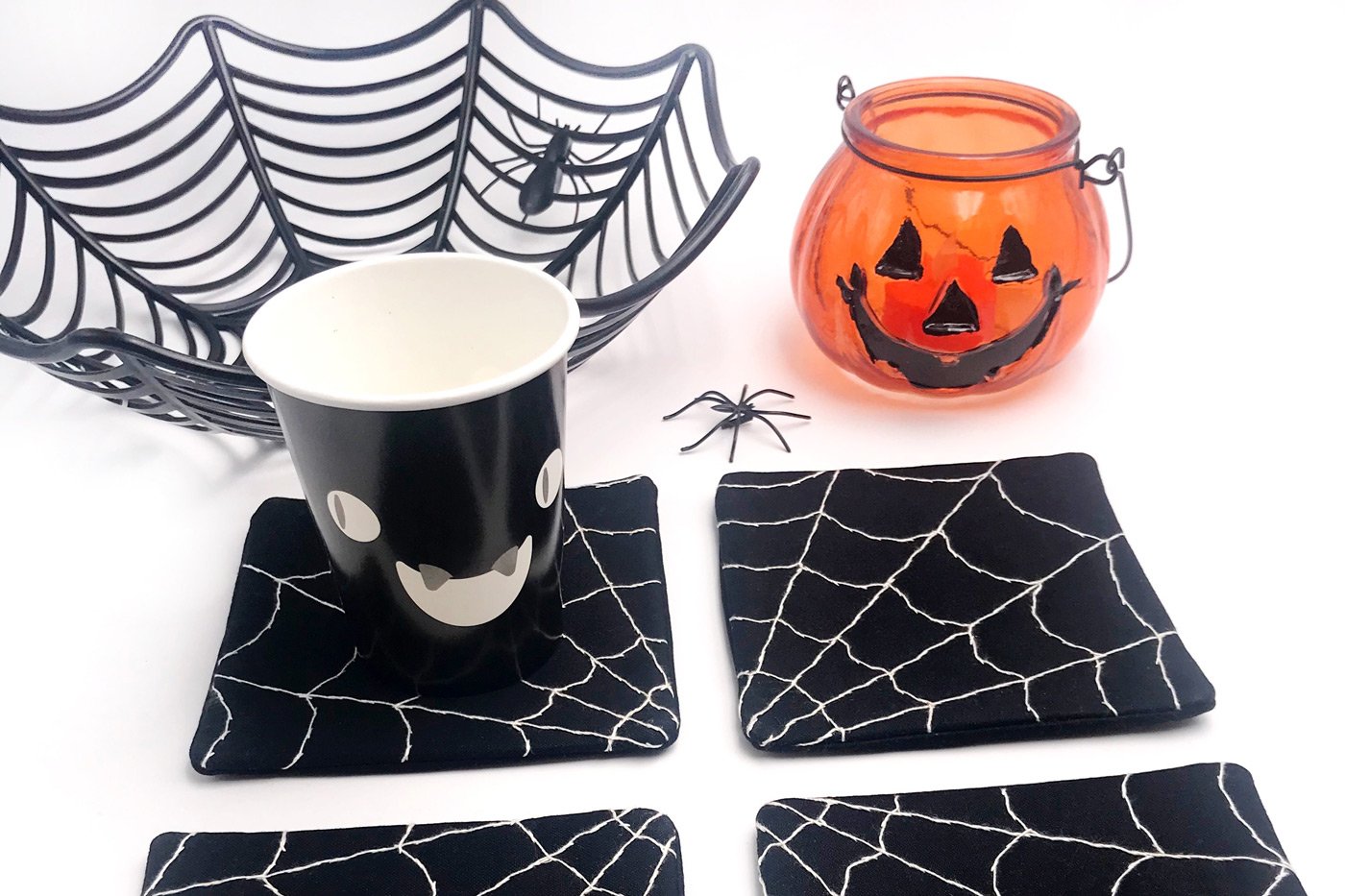 4 tatakan gelas laba-laba hitam dan putih di atas meja putih dengan alat peraga Halloween