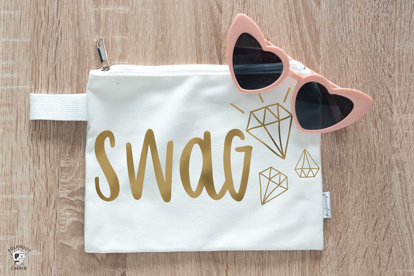 Fichier SVG Swag Cricut découpé avec du fer doré sur vinyle sur un sac blanc sur table avec des lunettes de soleil coeur rose