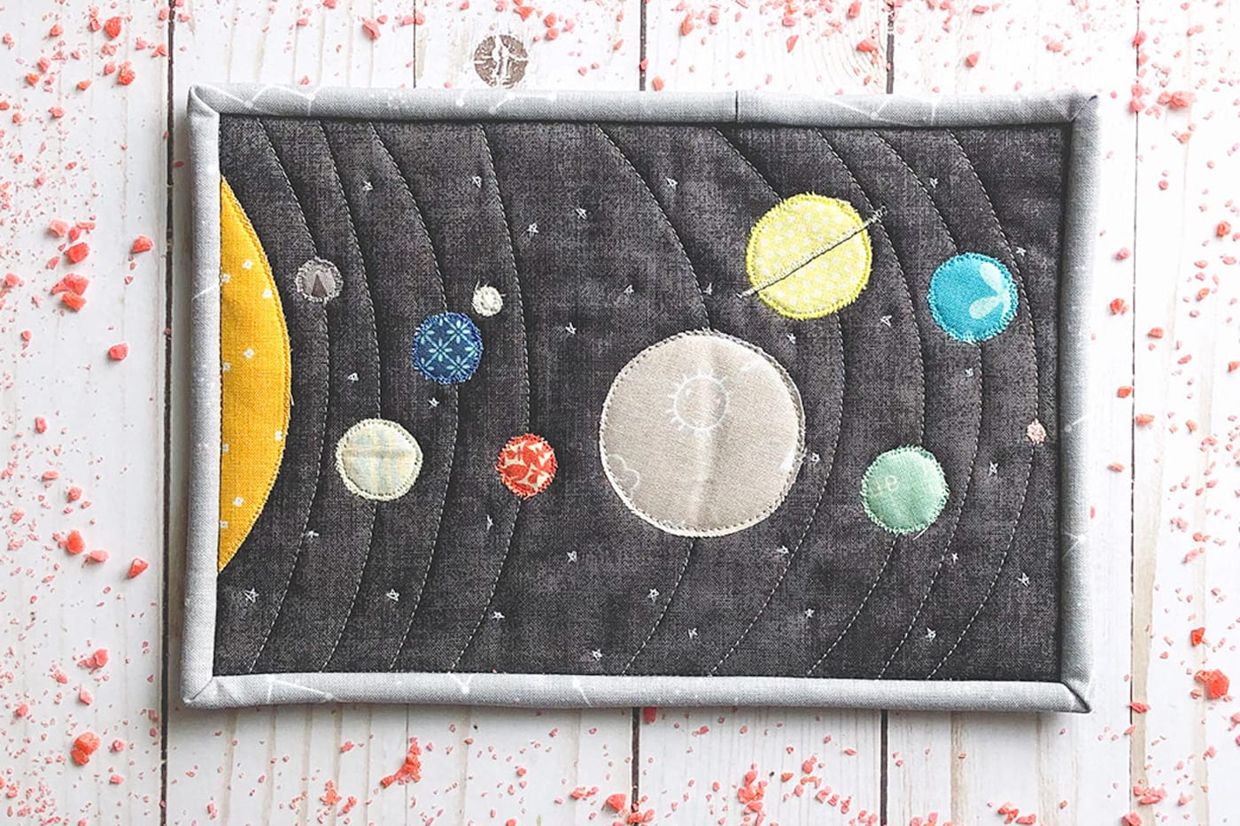 Tapis mug en tissu coloré du système solaire sur une table en bois blanc