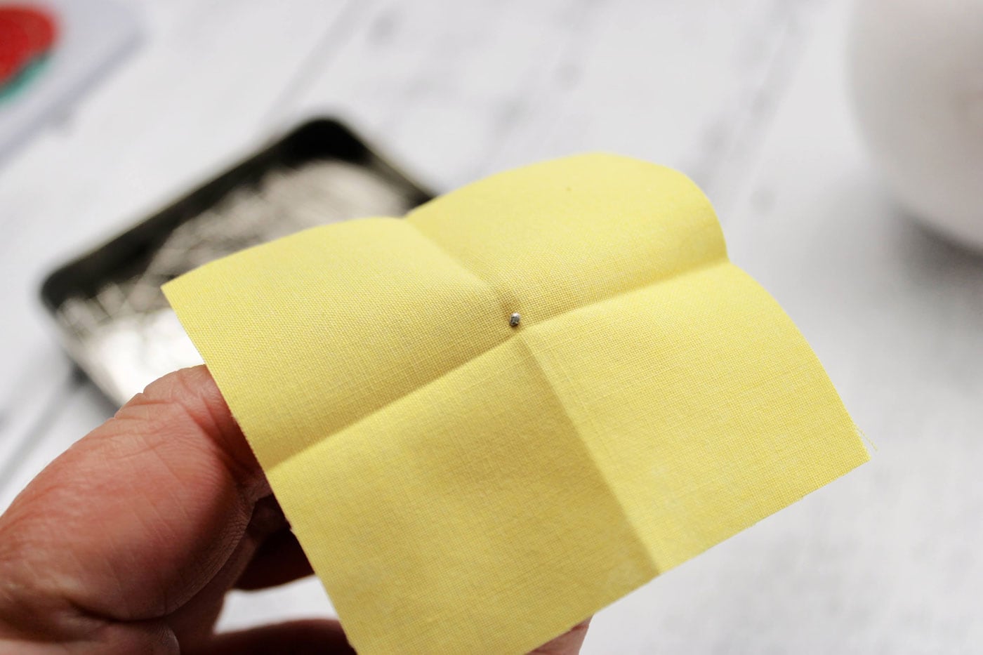 tissu jaune avec des plis, une épingle et une boule de polystyrène blanche